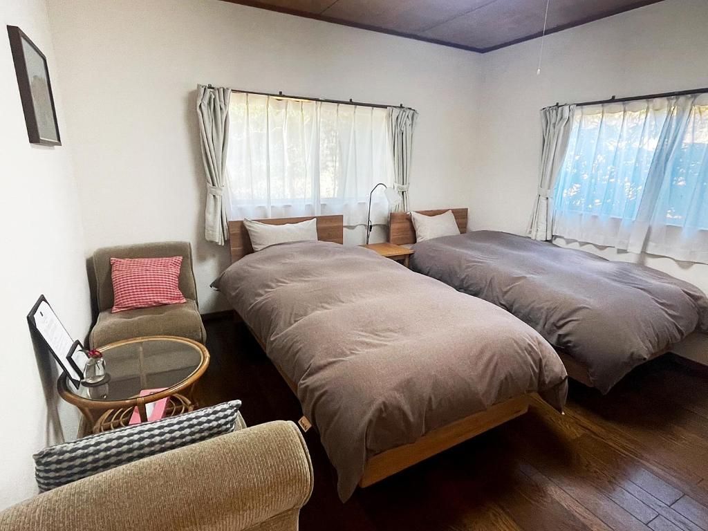 A room with two beds, a chair, a small table, and a window with curtains.