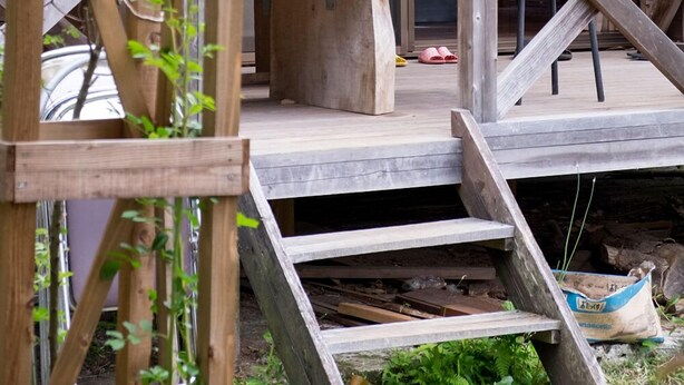 Een houten terras met een bankje, treden die naar een deur leiden en uitzicht op het interieur.