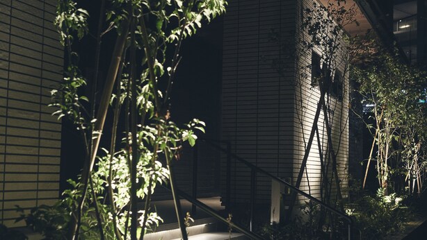 A staircase with a metal railing, surrounded by greenery and a building with a grid-like facade. - ReLA Higashimatsudo (Matsudo)