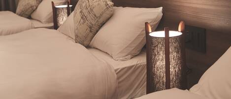 A hotel room with a wooden headboard, two bedside tables with lamps, and a bed with beige bedding and patterned pillows.