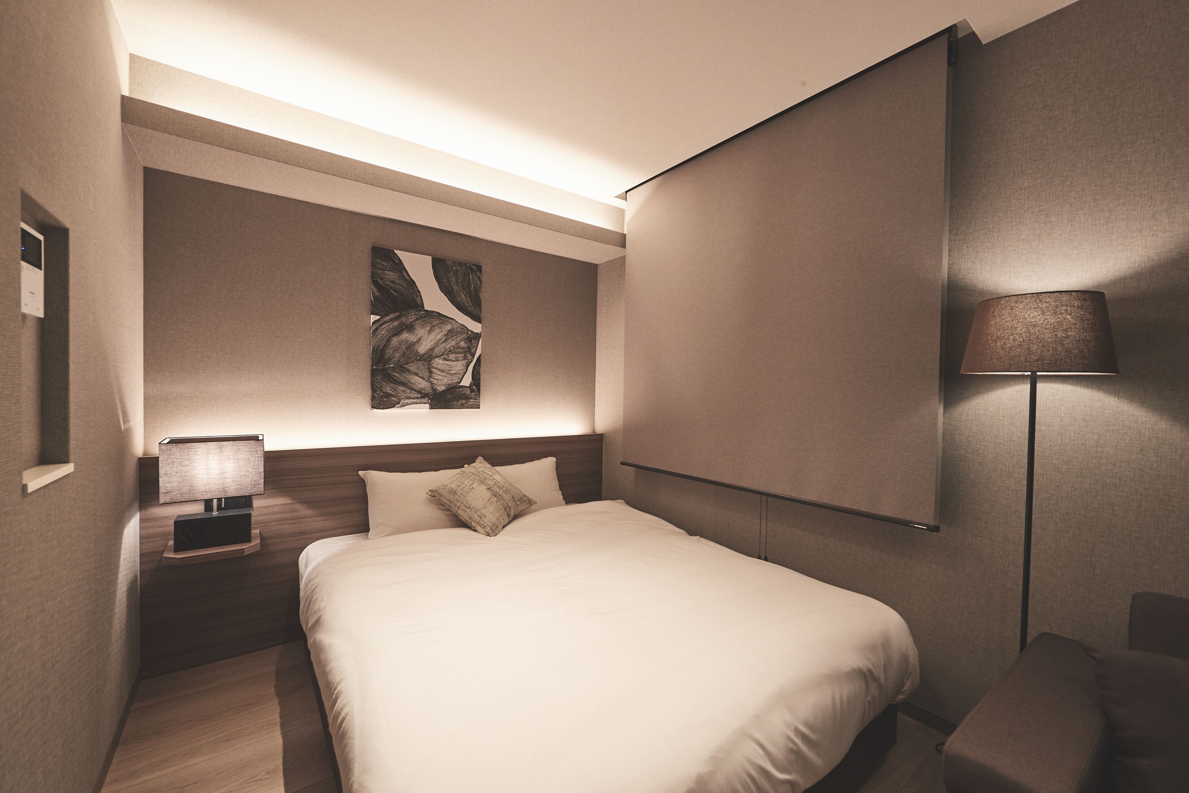 A modern hotel room with a large bed, a nightstand with a lamp, a wall-mounted TV, and a large window.