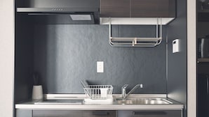 A modern kitchen with dark cabinetry, a stainless steel sink, and a dish rack. - ReLA Higashimatsudo (Matsudo)