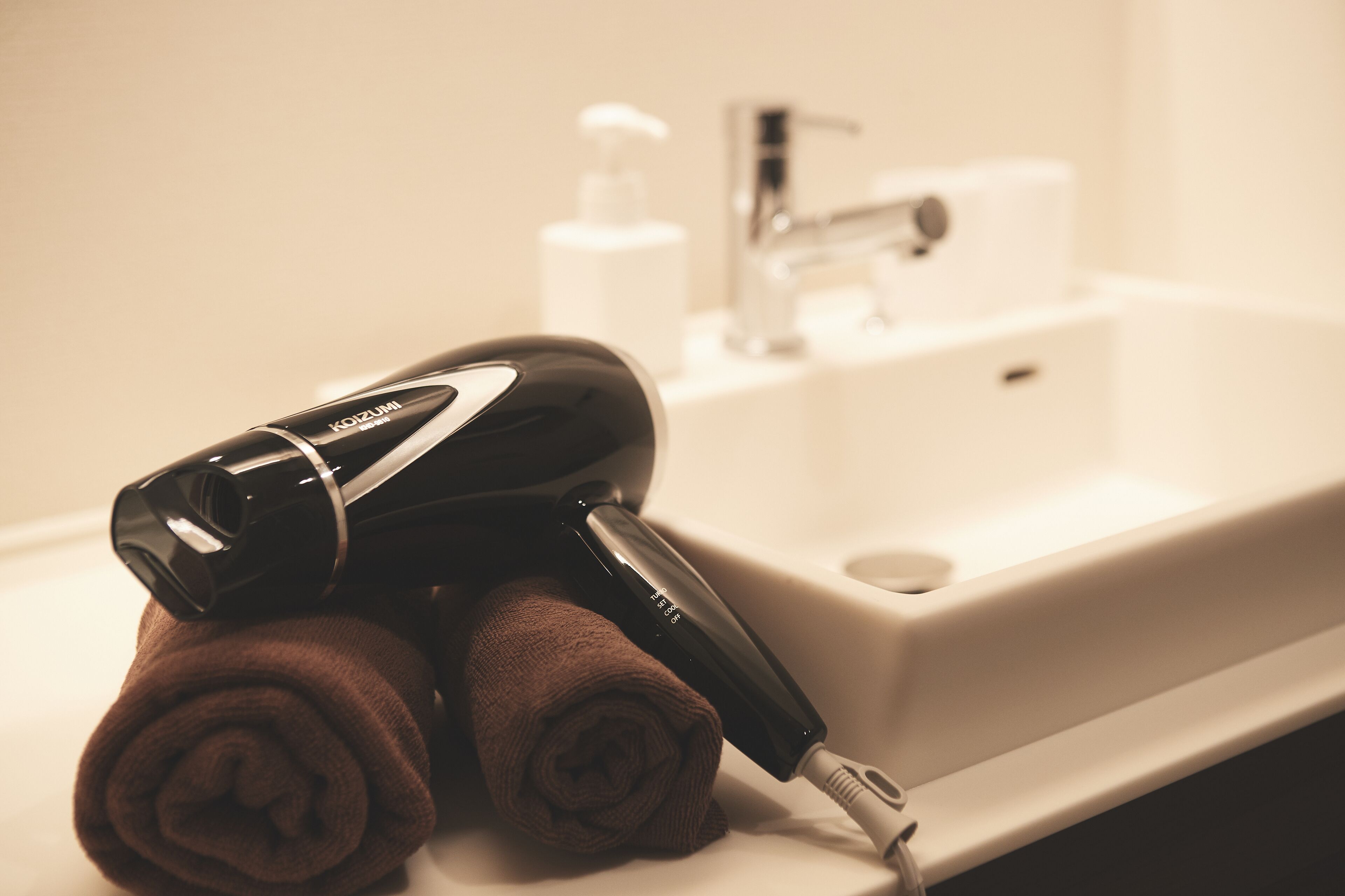 Une salle de bain avec un lavabo blanc, un sèche-cheveux et deux serviettes enroulées.