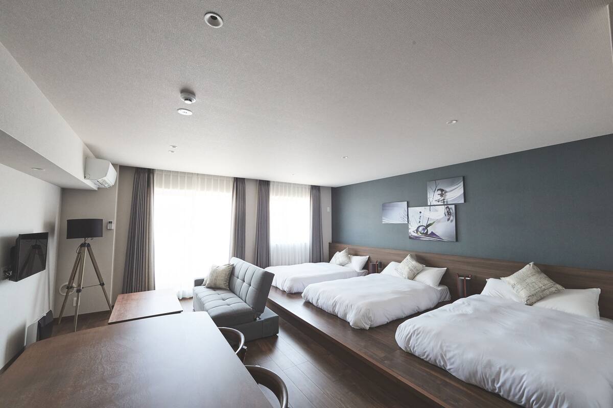 Une chambre d’hôtel avec deux lits, un bureau, une chaise, une télévision et un trépied.