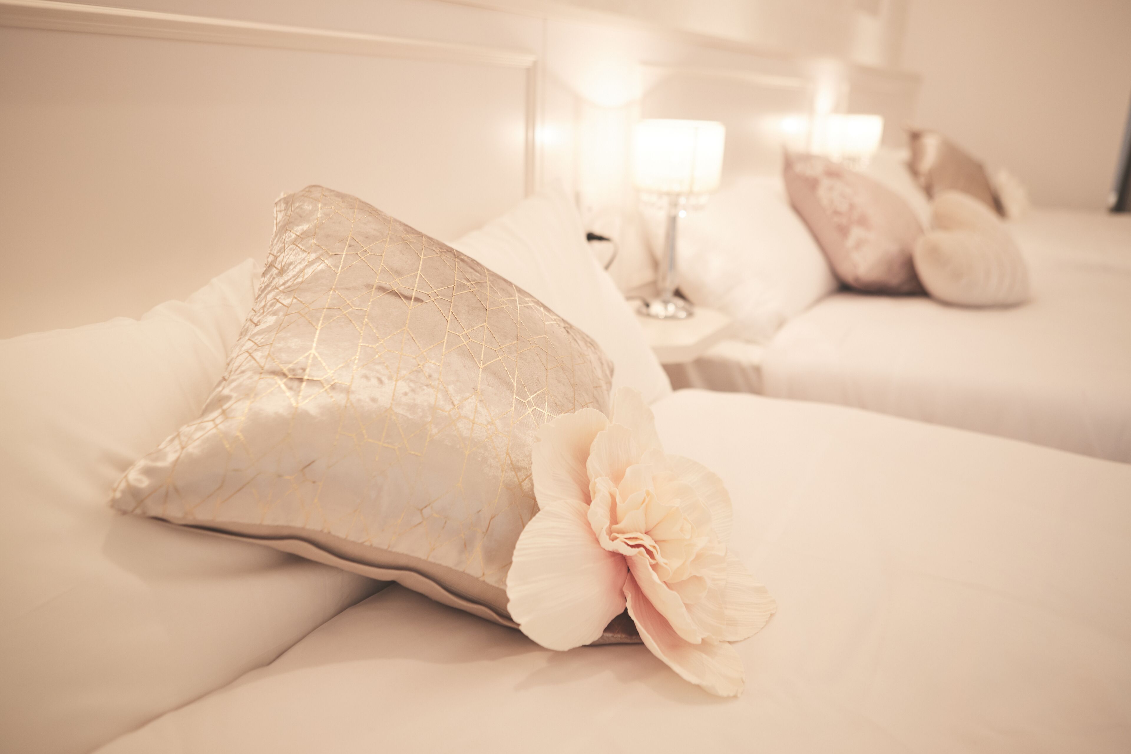 A hotel room with two beds, each with white bedding and decorative pillows. There is a nightstand with a lamp between the beds.
