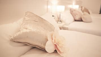 A hotel room with two beds, each with white bedding and decorative pillows. There is a nightstand with a lamp between the beds.