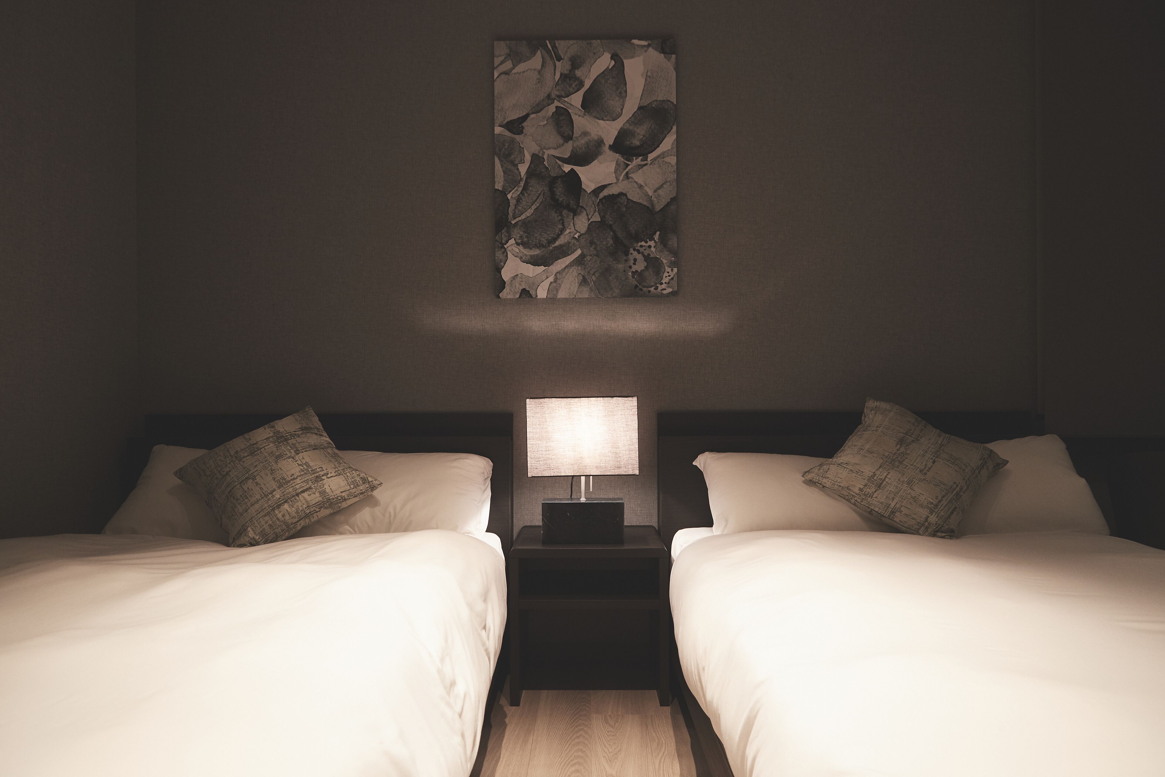 A twin room with two beds, a nightstand with a lamp, and a wall-mounted artwork.