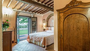 Ein Schlafzimmer mit einem Bett, einer Holztür, einem Fenster und Blick ins Freie.