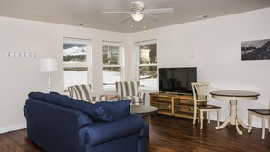 Un salon avec un canapé bleu, une table à manger avec des chaises, un téléviseur et de grandes fenêtres donnant sur un paysage enneigé.