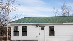 Une maison de plain-pied avec un toit en métal vert, un revêtement extérieur blanc et une porte d’entrée.