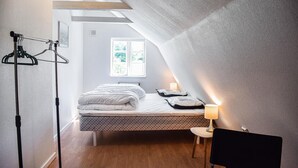 Ein gemütliches Schlafzimmer mit Bett, kleinem Tisch, Stuhl und einem Fenster mit Tageslicht.