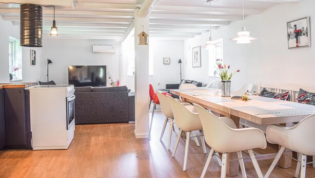 Ein modernes Wohnzimmer mit Fernseher, Sofa und Essbereich mit Stühlen.