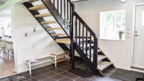 Eine Treppe mit schwarzen Geländern und Holzstufen, die zu einer Empfangshalle mit einer kleinen Bank und einem Fenster mit Blick auf Grünanlagen führt.