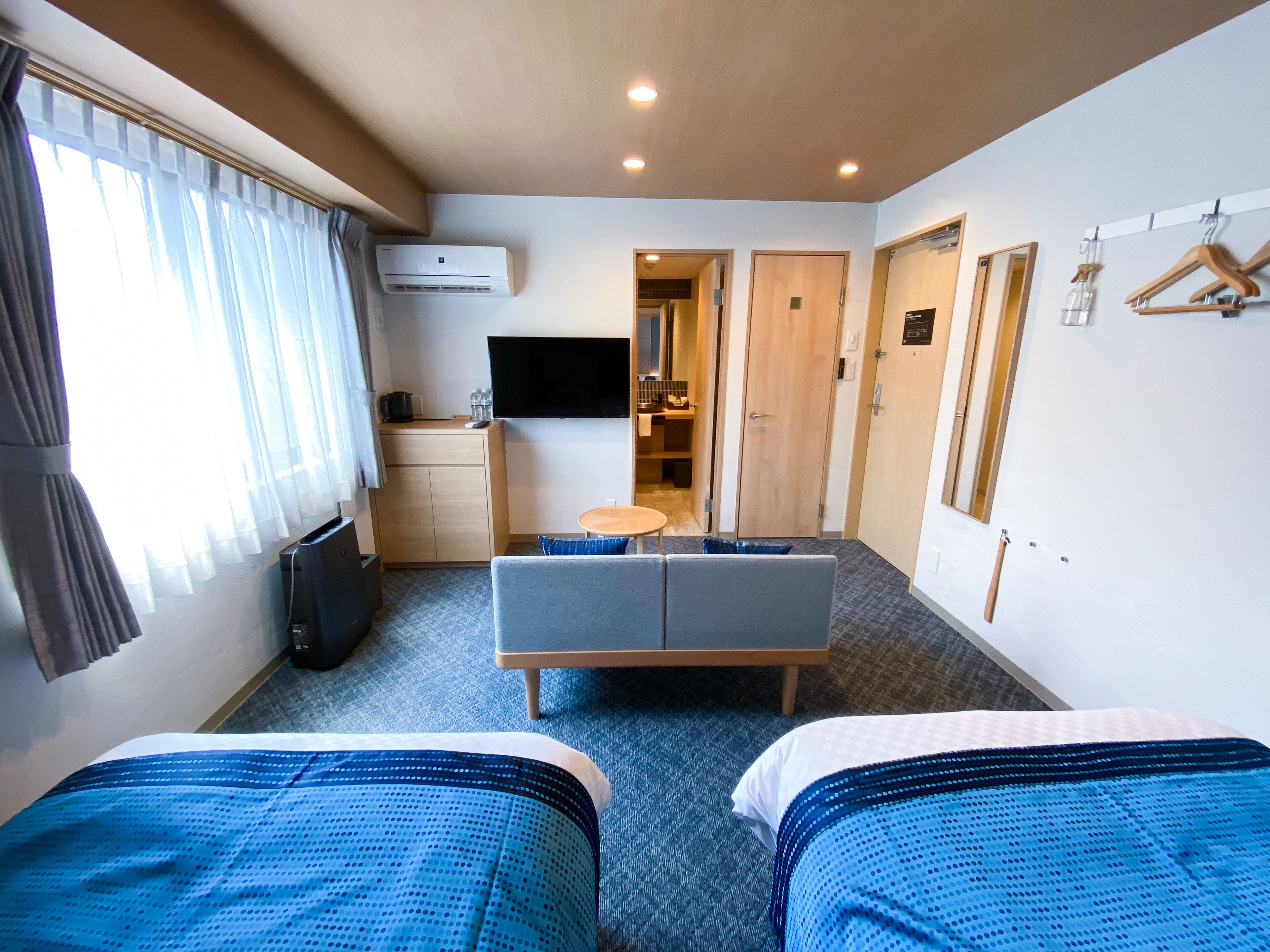 A hotel room with two beds, a desk, a TV, and a bathroom visible through an open door.