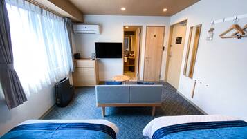 A hotel room with two beds, a desk, a TV, and a bathroom visible through an open door.