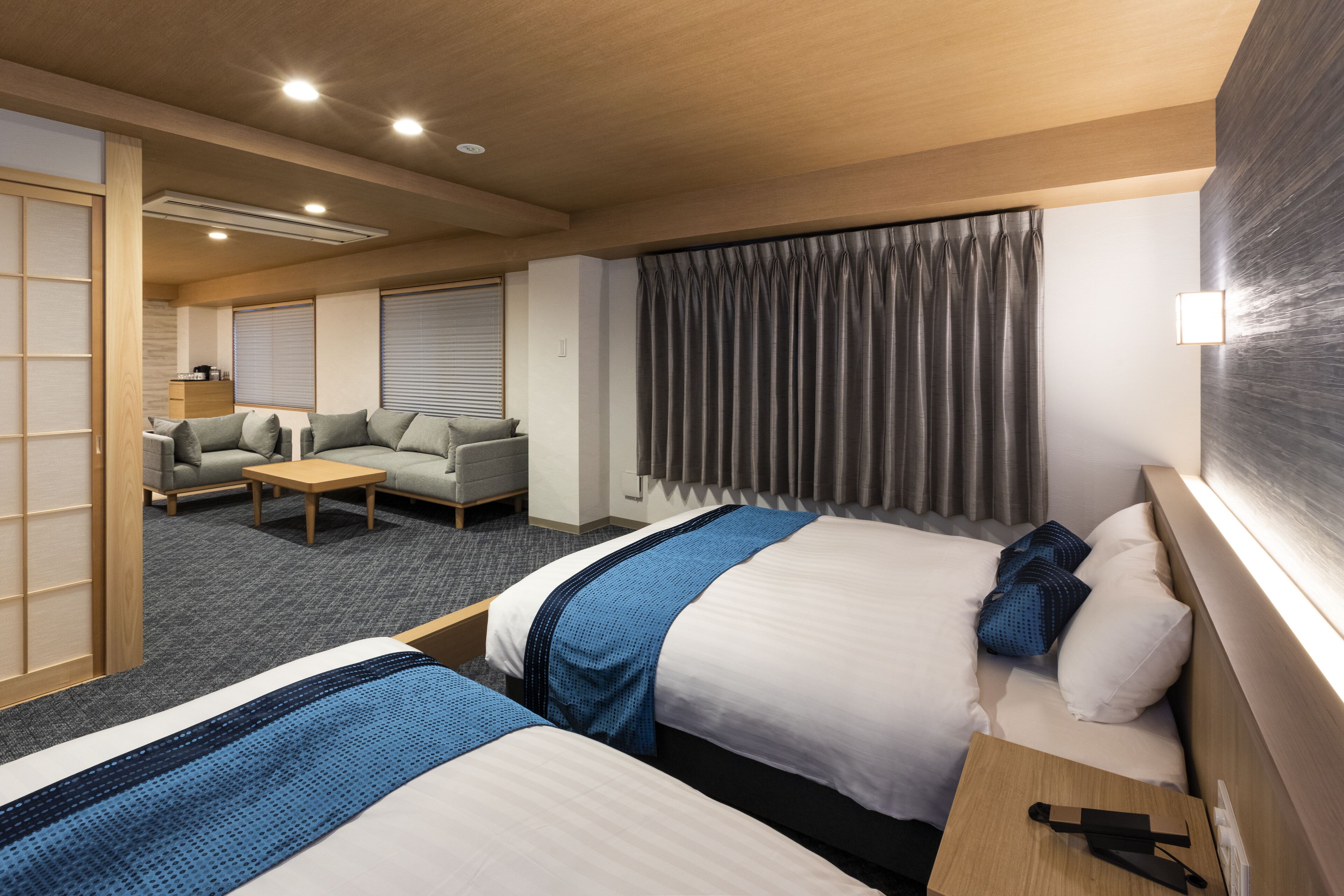 Habitación de hotel con dos camas, un sofá, una mesa de centro y un ventanal con cortinas.