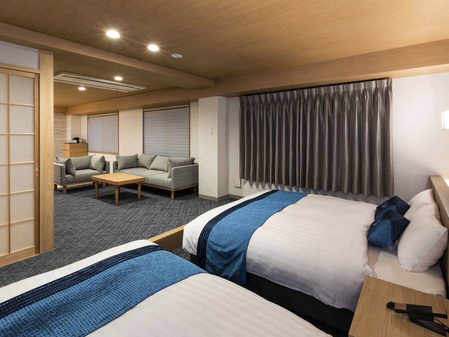 Habitación de hotel con dos camas, un sofá, una mesa de centro y un ventanal con cortinas.