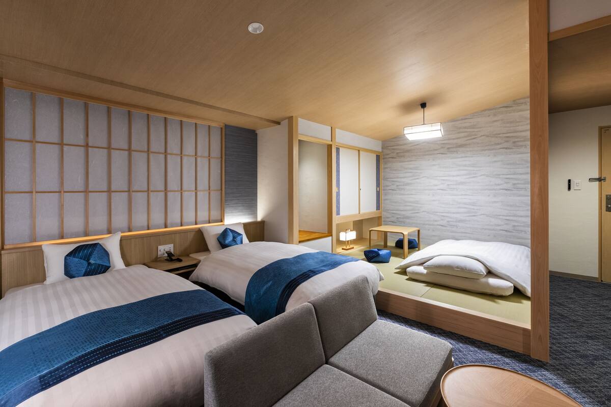 A hotel room with two beds, a sofa, a desk, and a wardrobe.