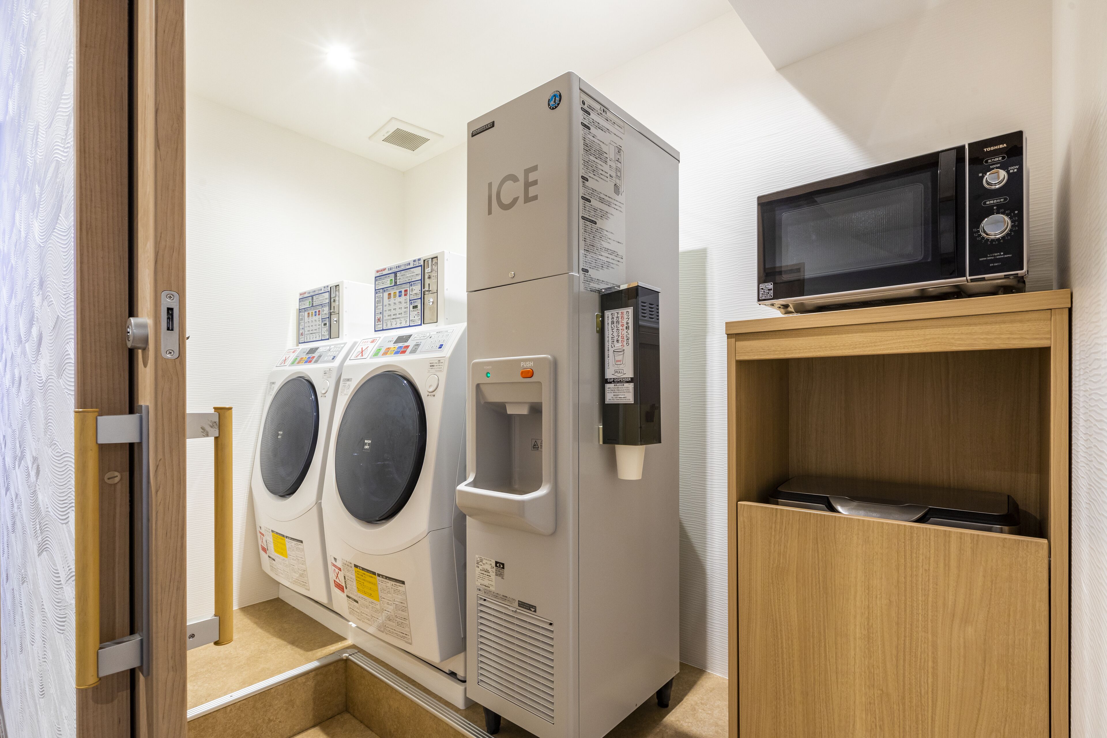 Une buanderie équipée de deux machines à laver, d’un distributeur d’eau et d’un four à micro-ondes, le tout installé sur une étagère en bois.