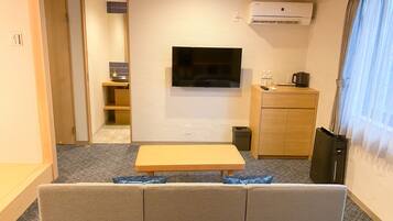 A modern living room with a sofa, a flat-screen TV, a small table, a cabinet, and an air conditioning unit.
