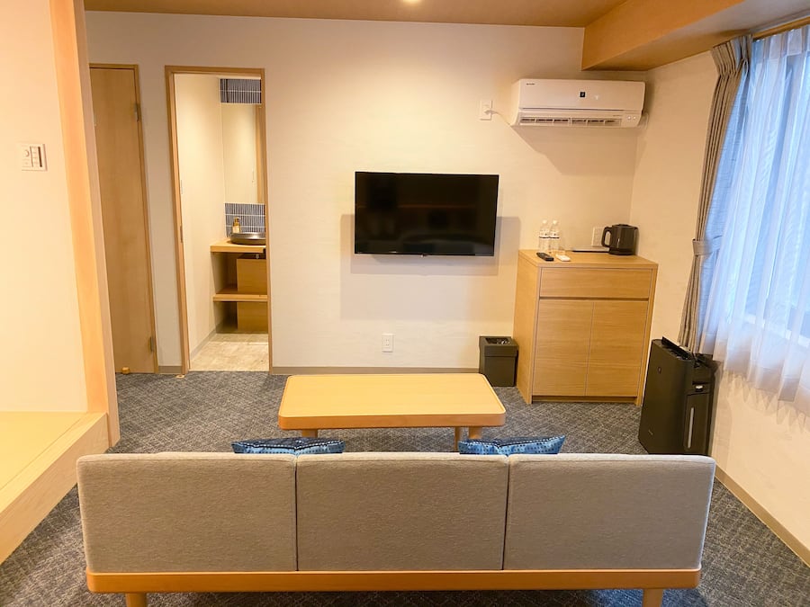 A modern living room with a sofa, a flat-screen TV, a small table, a cabinet, and an air conditioning unit.