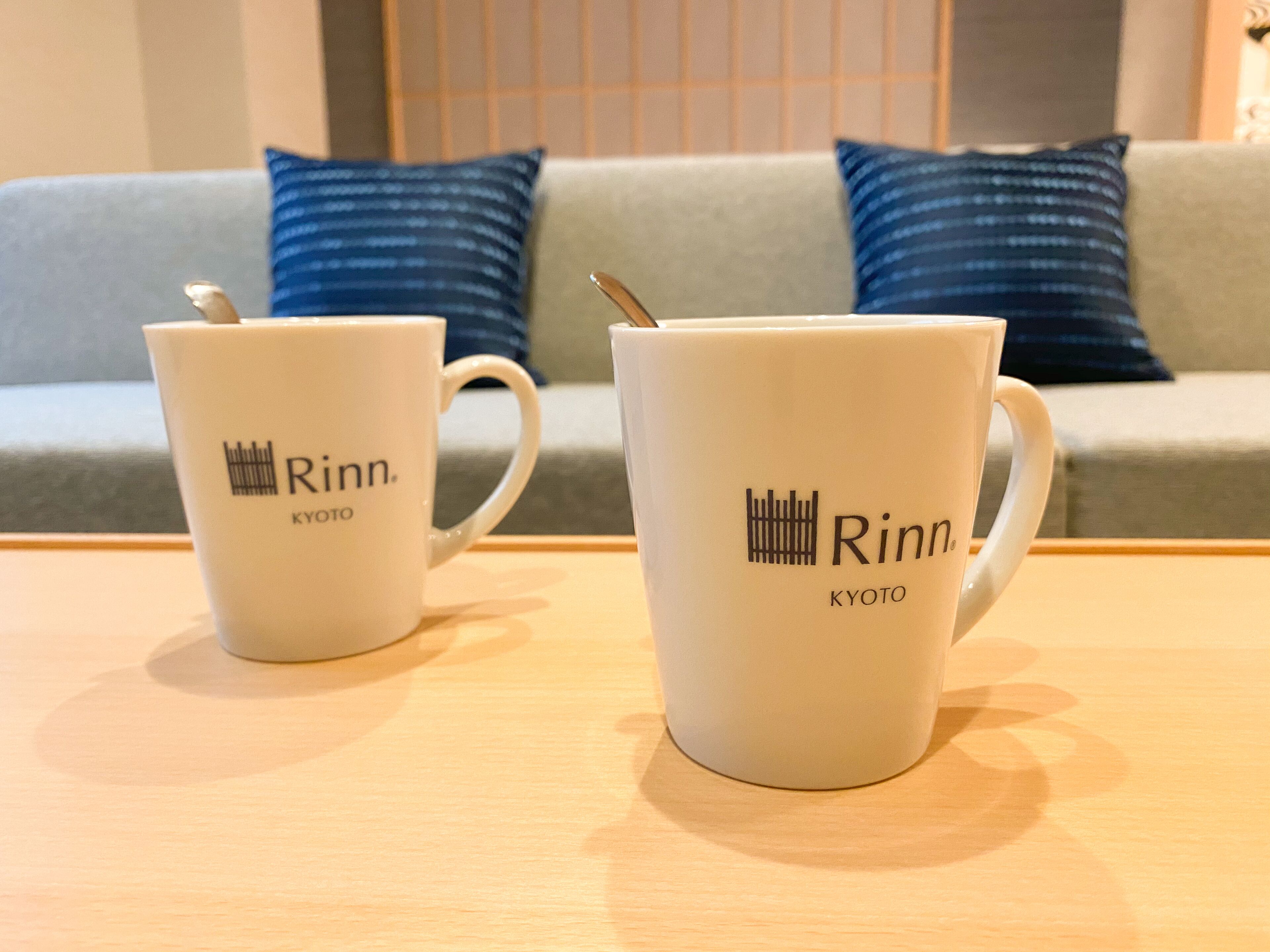 Two white mugs with the logo 'Rinn Kyoto' on a wooden table.
