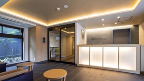 A reception area with a modern design, featuring a reception desk, seating area with tables and chairs, and a large window providing natural light.