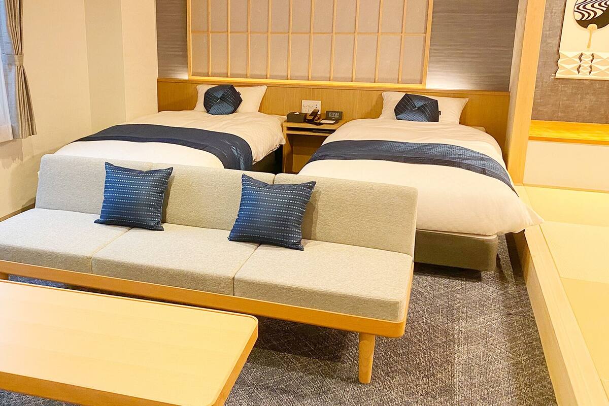 A hotel room with two beds, a sofa, a small table, and a window with curtains.