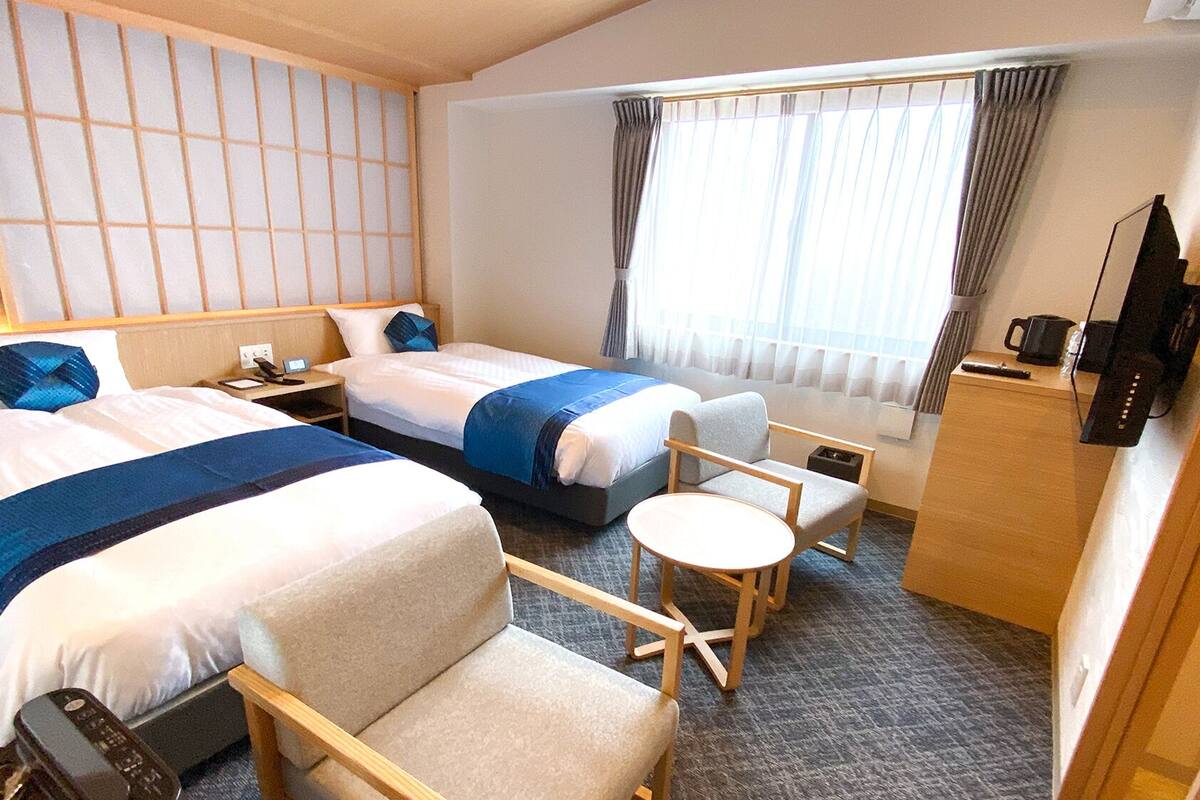 A hotel room with two beds, a small table, a chair, a desk, and a TV.