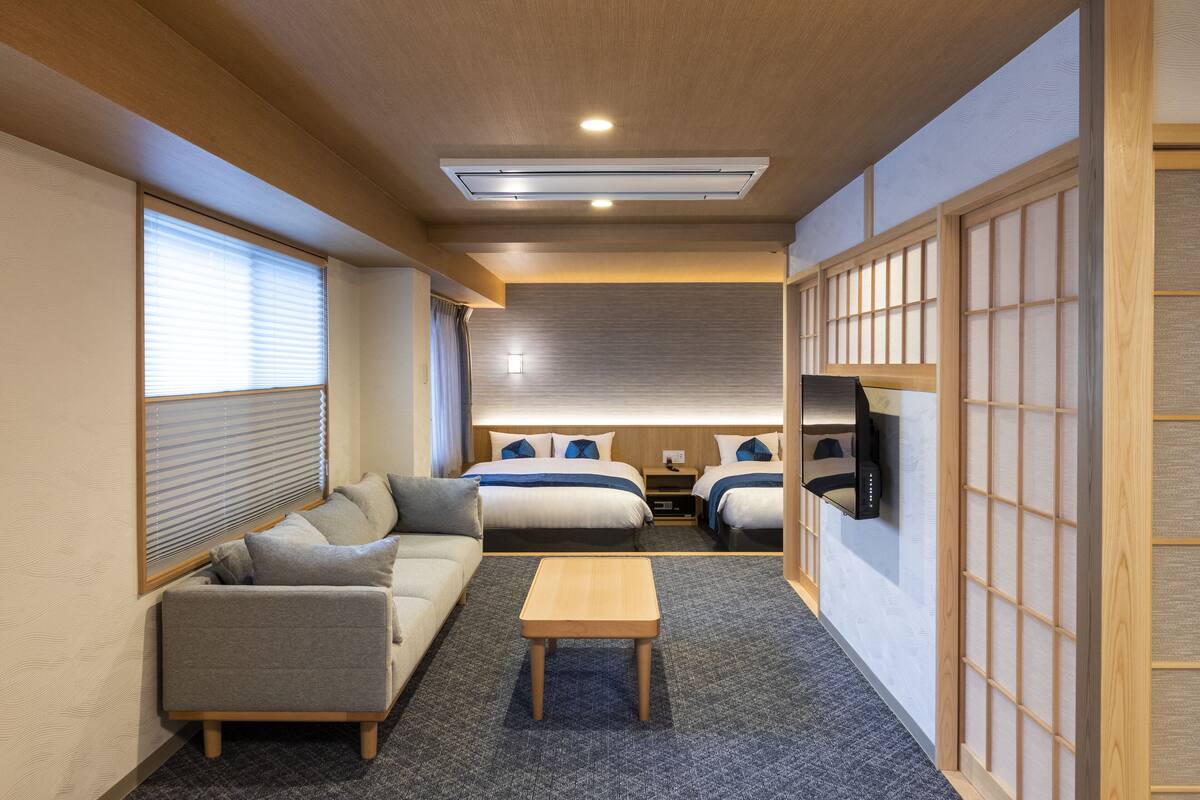 A hotel room with a sofa, two beds, a TV, and a small table.