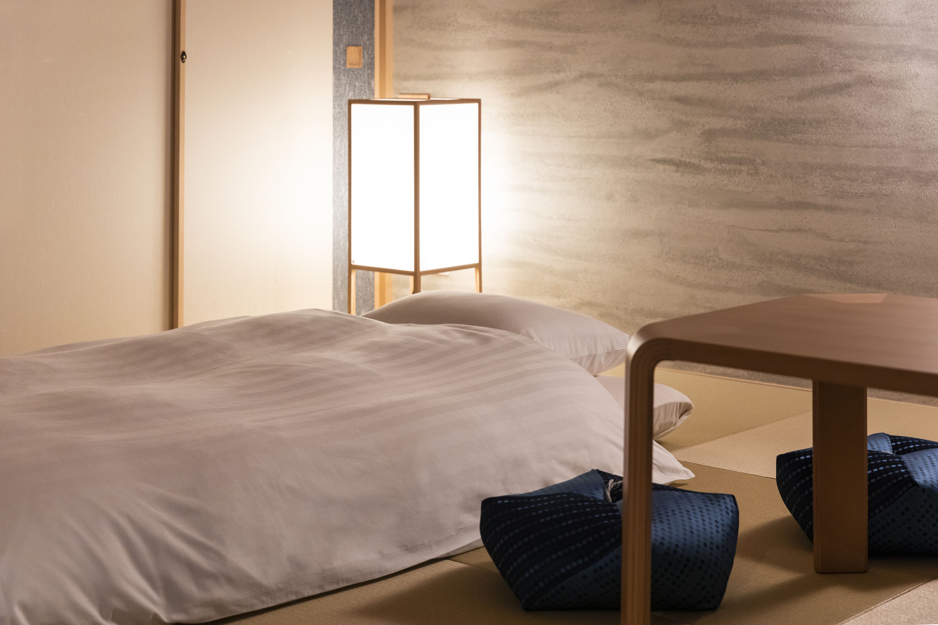 A hotel room with a bed, a wooden table, and a tatami mat floor.
