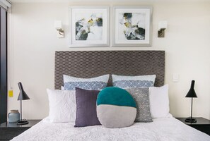 A neatly made bed with patterned pillows, a decorative headboard, and two framed abstract paintings on the wall.