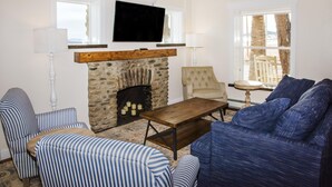 A living room with a stone fireplace, a television mounted above it, striped blue and white sofas, and a wooden coffee table.