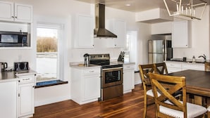 A modern kitchen with white cabinetry, a stainless steel refrigerator, a built-in oven, and a large dining table with wooden chairs.