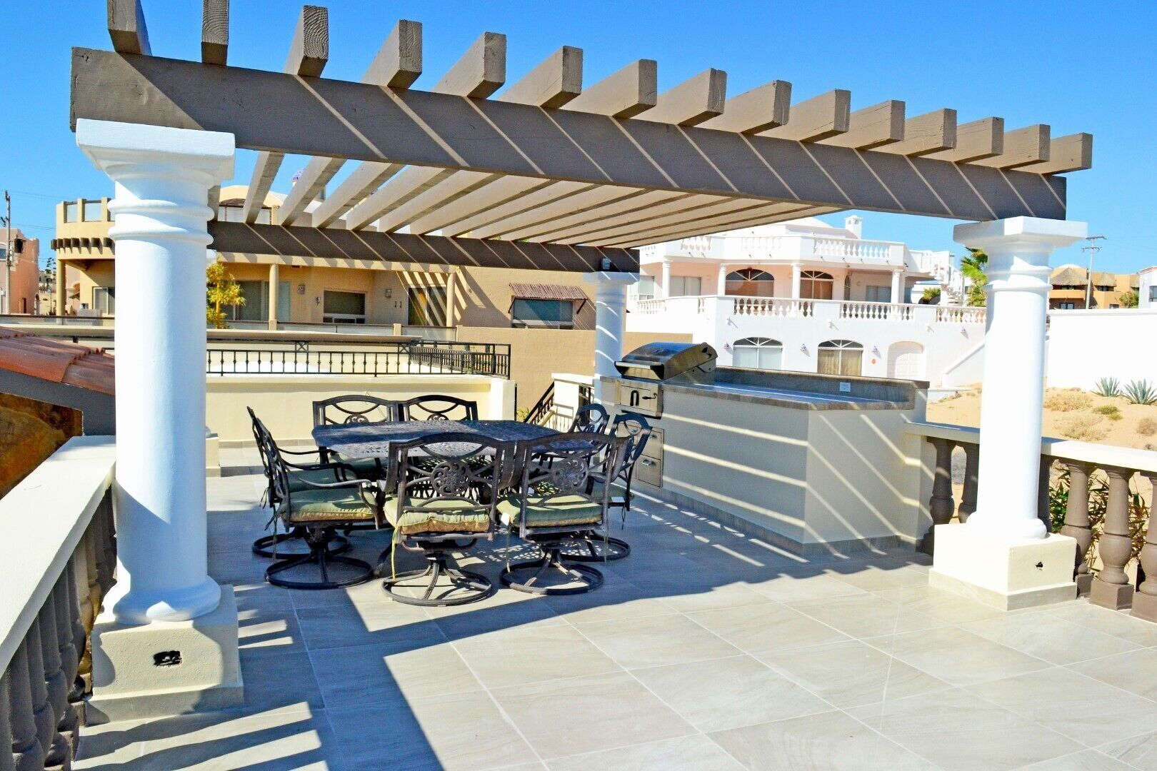 An outdoor patio with a pergola, a table with chairs, and a grill.