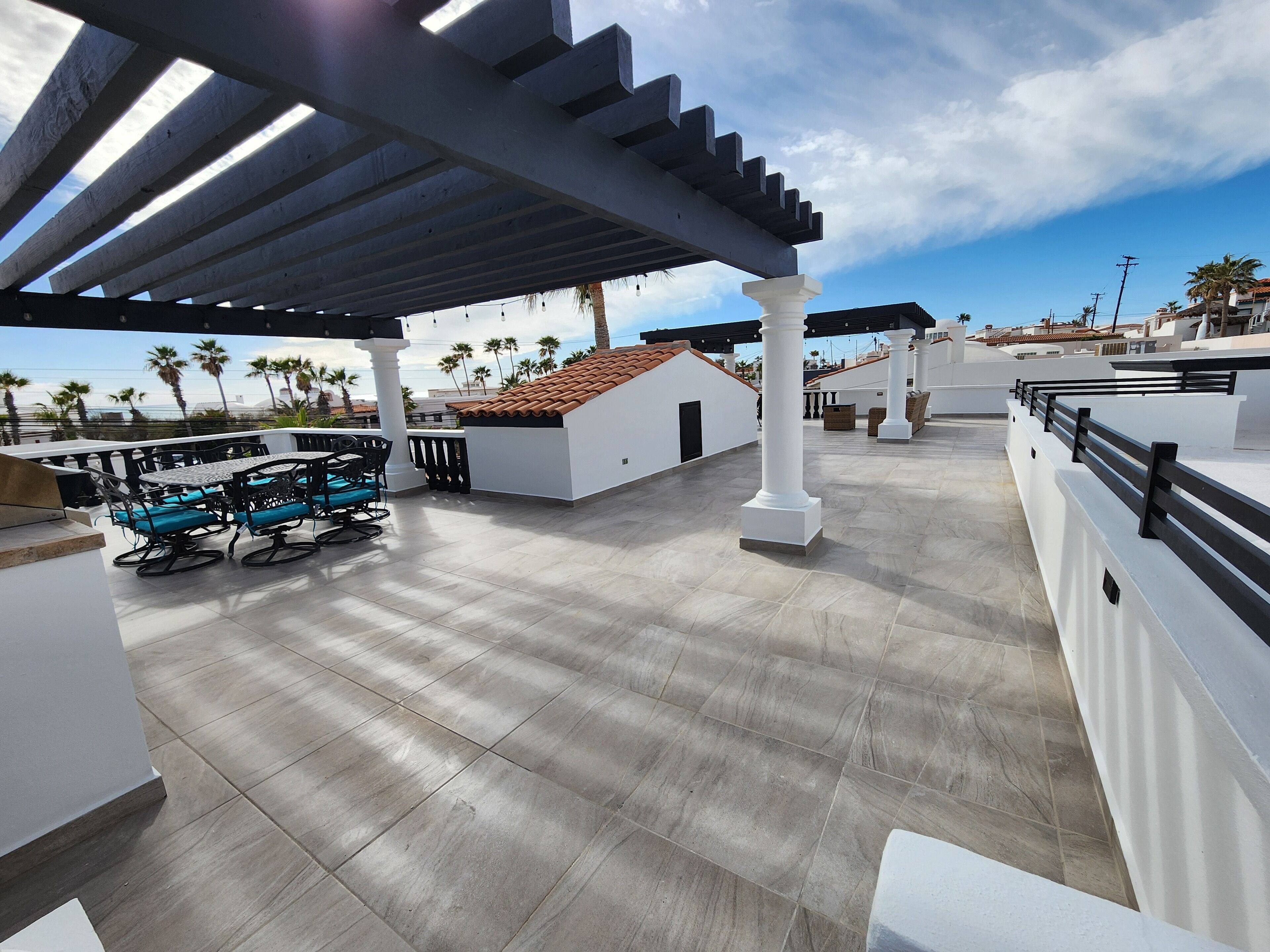 A rooftop terrace with a pergola, outdoor seating, and a view of palm trees and buildings.