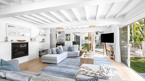 Relax in this stylish living room with a large sofa, armchair, and fireplace, offering a peaceful retreat with a balcony overlooking a lush garden and pool.