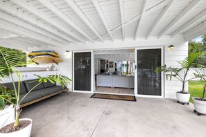 A modern living space with a grey sofa, a dining area with a table, and a kitchen area with surfboards mounted on the wall.