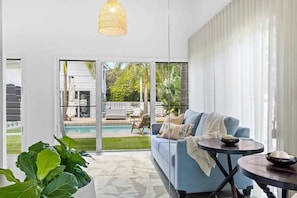 A modern living room with a blue sofa, a round coffee table, and a large window overlooking a pool and garden.