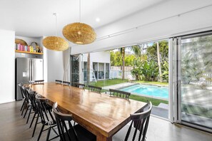 A modern kitchen with a large wooden dining table, black chairs, and two wicker pendant lights.