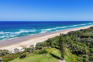 A coastal landscape with a beach, ocean, and dense greenery.
