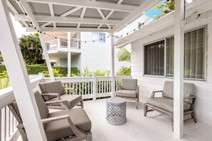 A covered outdoor seating area with white railings, multiple chairs, and a round table.