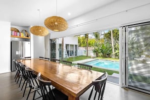 Une cuisine moderne avec une grande table à manger en bois, des chaises noires et une vue sur une piscine.