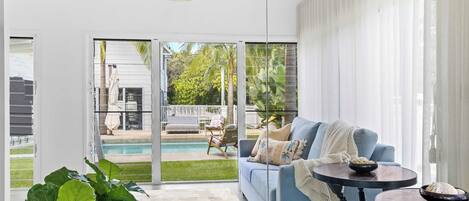 A modern living room with a blue sofa, a round table, and a view of a pool and outdoor furniture.