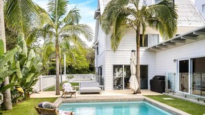 A backyard with a swimming pool, palm trees, a white house, and a covered patio area. - Barra Luxe Beach House 4BR Yaroomba (Point Arkwright)