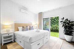 A bedroom with a bed, bedside tables, a large window, and a potted plant.