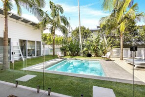 A backyard with a swimming pool, palm trees, and a deck with lounge chairs.