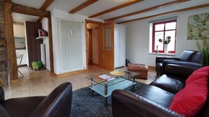 Un salón con una mesa de centro de vidrio, sofás de cuero, un cojín rojo, techo de madera y una ventana con una planta.