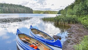 Dos canoas con remos amarradas en un lago tranquilo, rodeado de vegetación exuberante y un bosque al fondo.
