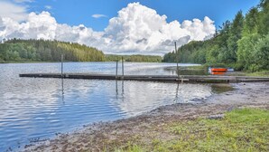 Un lago tranquilo con un muelle de madera que se adentra en el agua, rodeado de un bosque frondoso y un cielo despejado.